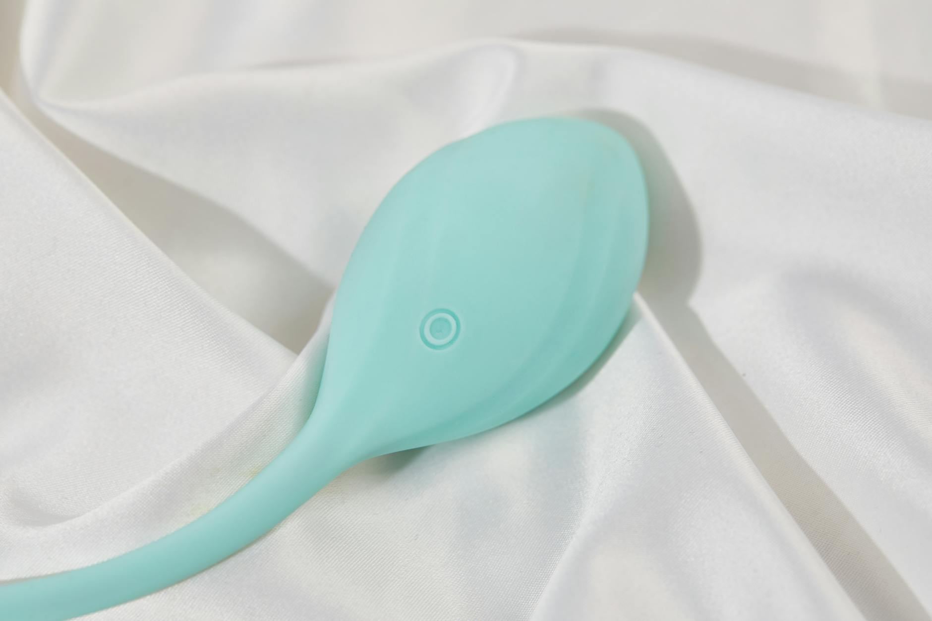 A teal clitoral vibrator resting on white silk fabric, symbolizing luxury and personalized pleasure