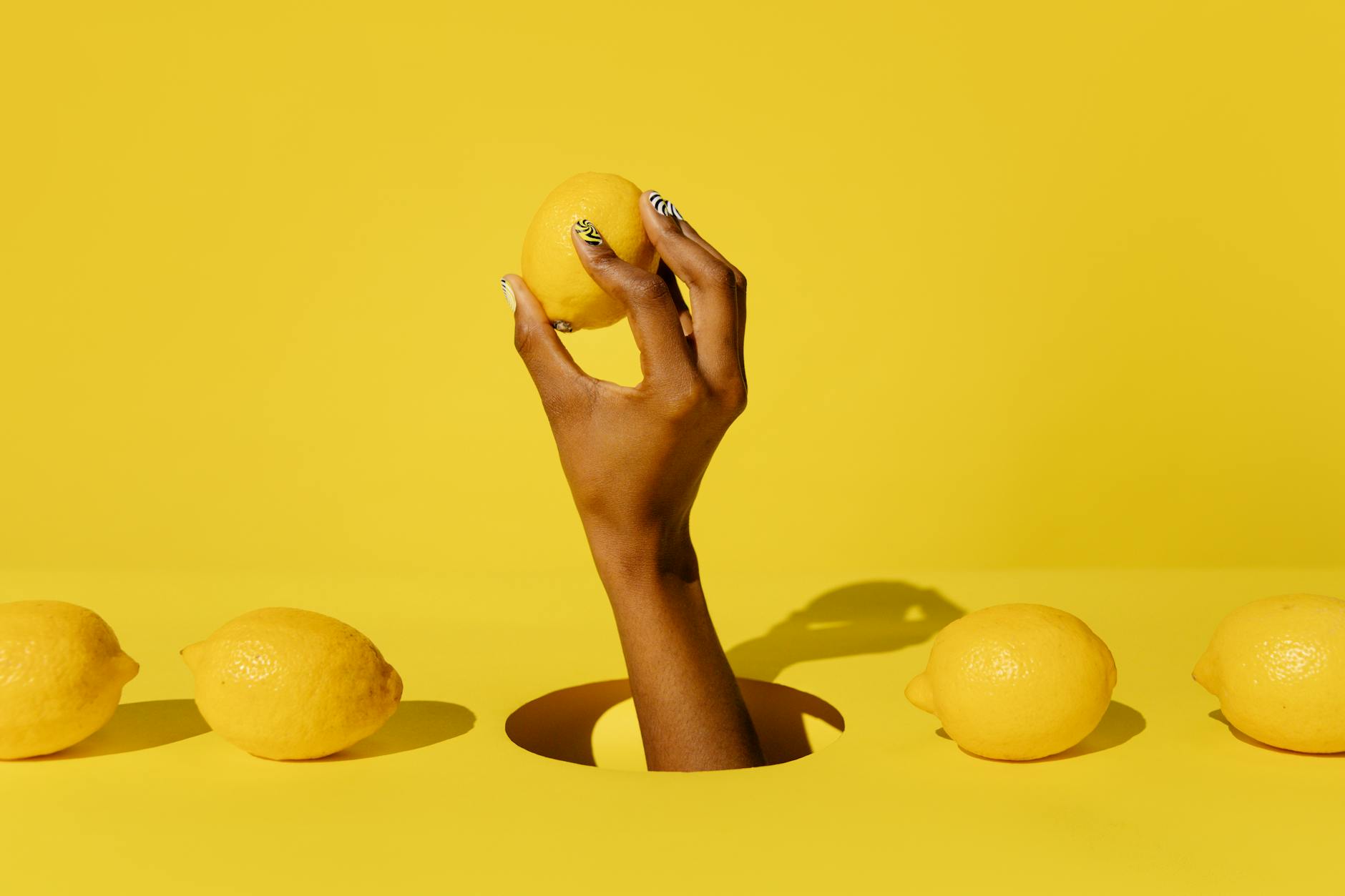 A hand holding a fresh lemon against a bright yellow background, symbolizing the citrus-inspired design of lemon vibrators