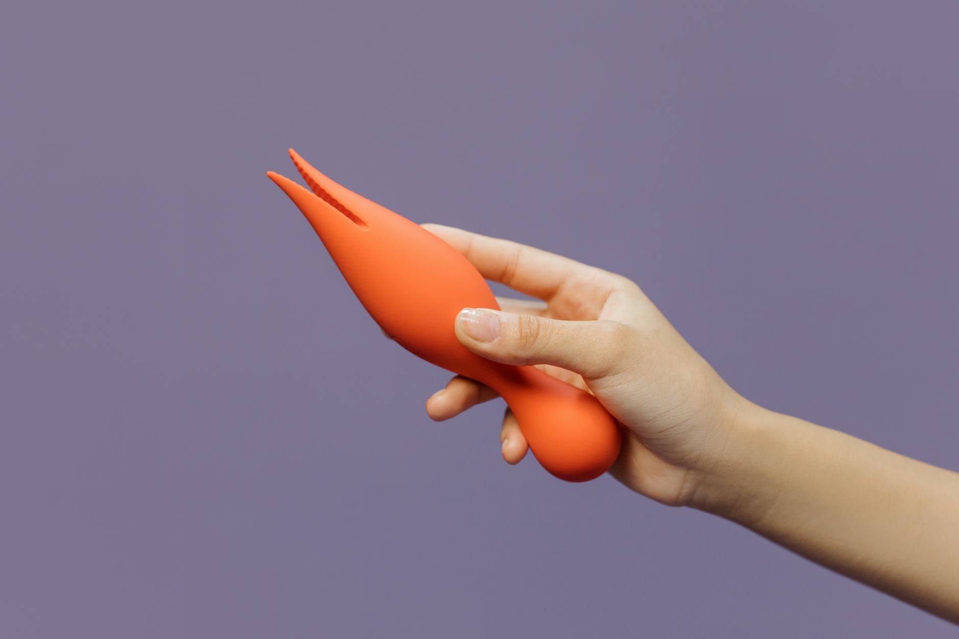 Hand holding a lemon-colored vibrator against a minimalist purple background, representing modern sexual wellness