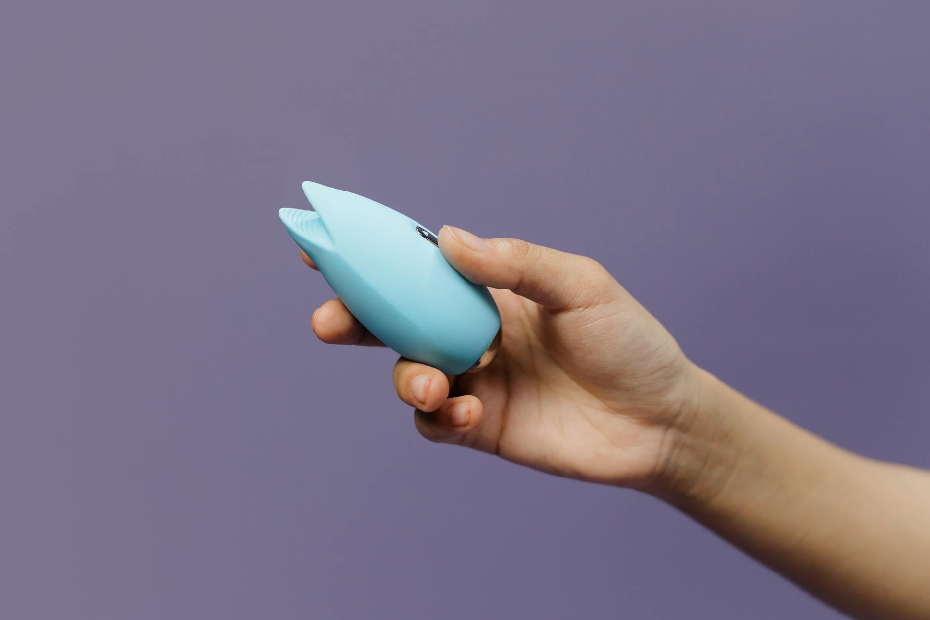 A silicone clitoral vibrator held in hand against a purple background, representing self-pleasure and intimate wellness