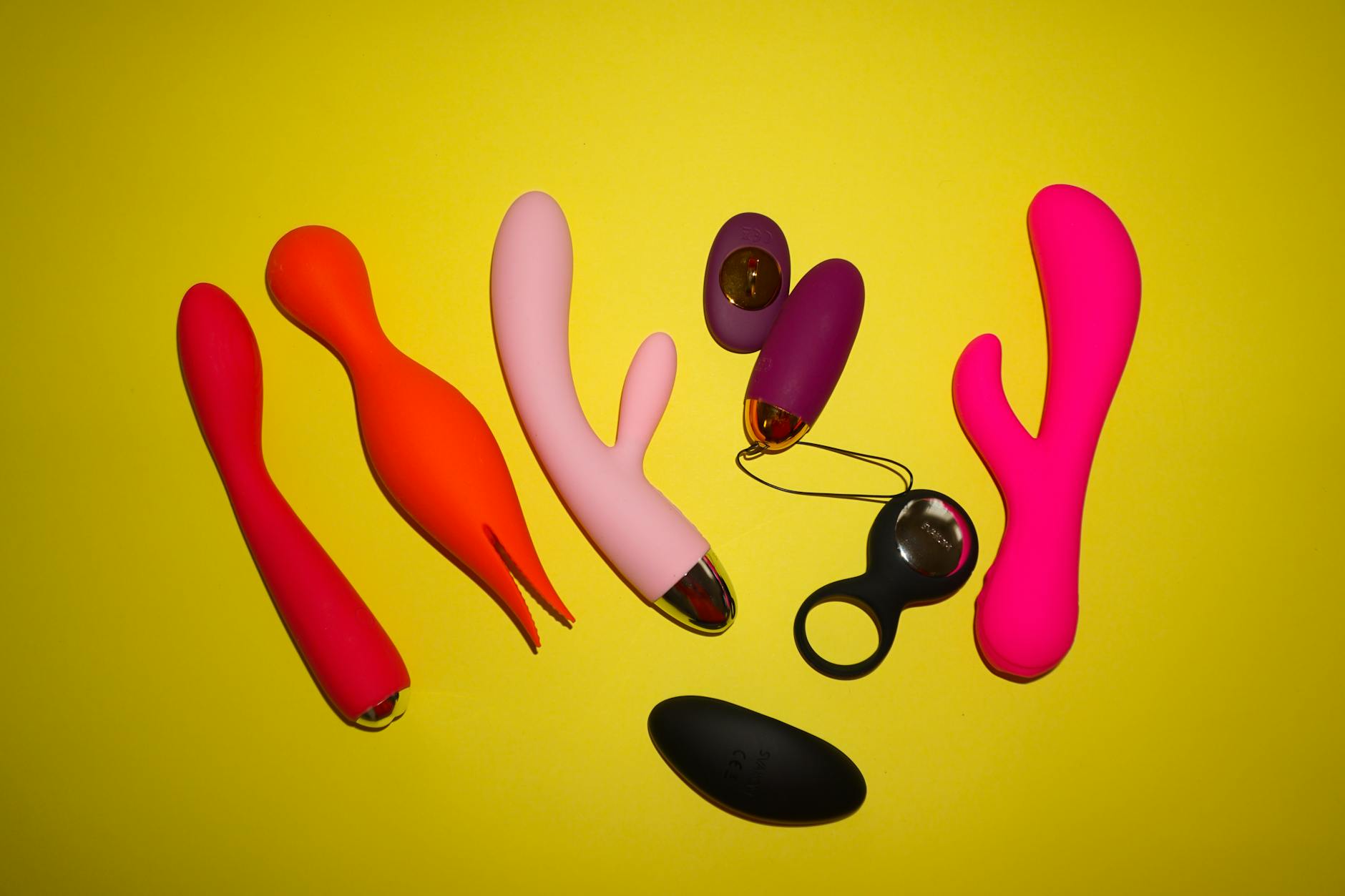 Two hands holding pink and blue silicone vibrators against a pastel background